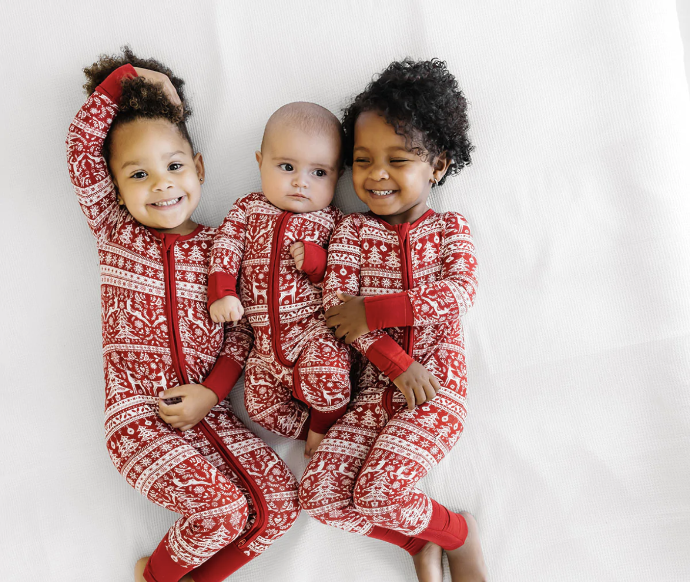 Three babies laying together on white bedsheet