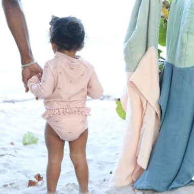 baby at the beach, with an adult holding her hand