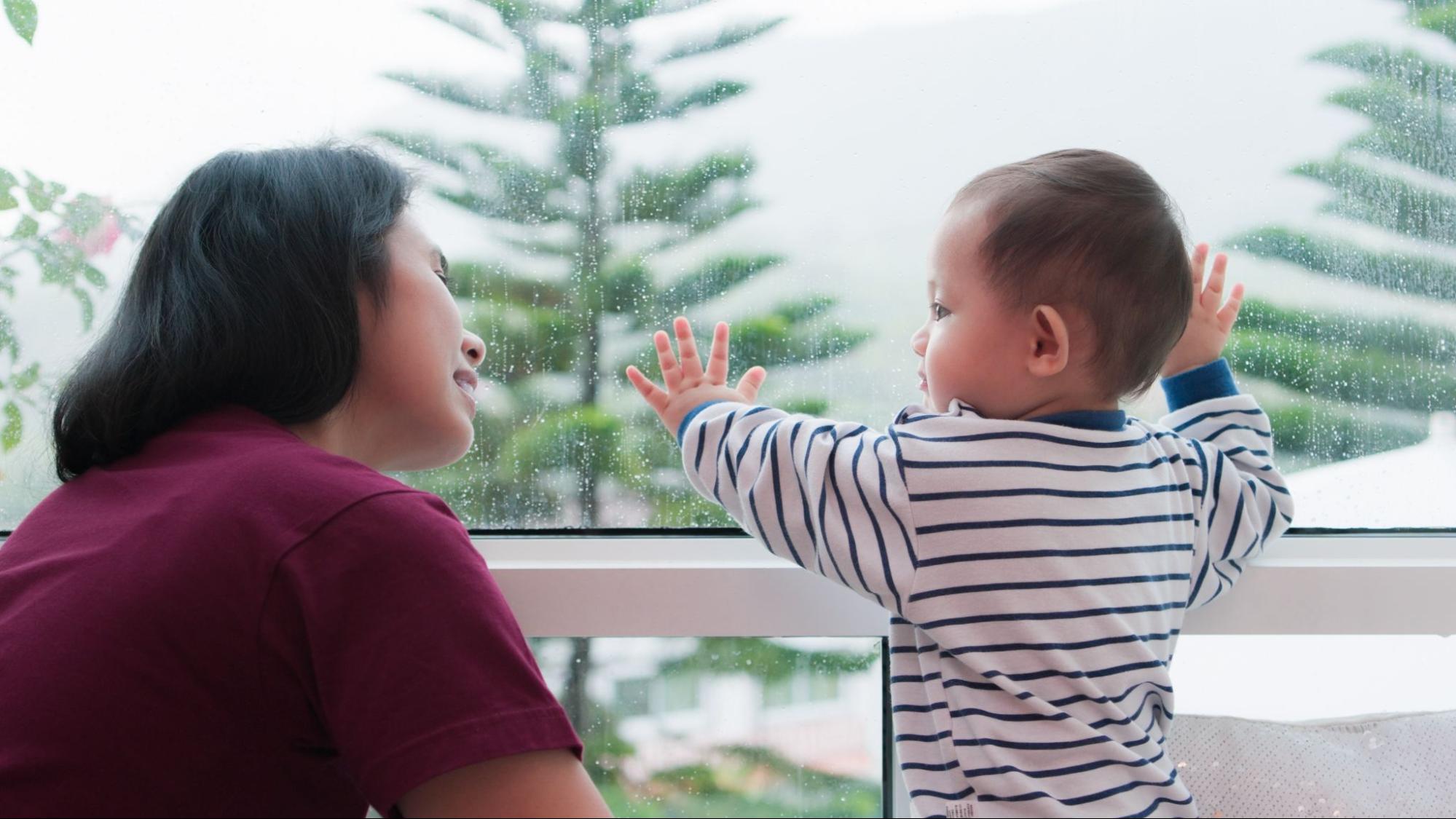 Mom and baby looking out a rainy window