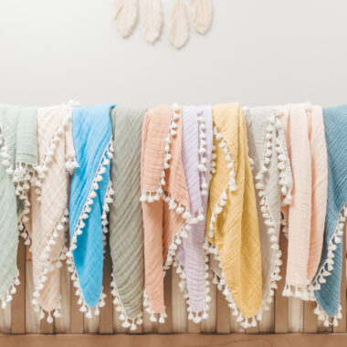 Variety of pastel baby blankets hanging on a crib