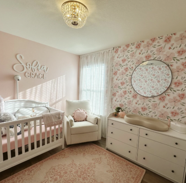 Corner of a pink floral nursery with a crib, glider and baby changing table