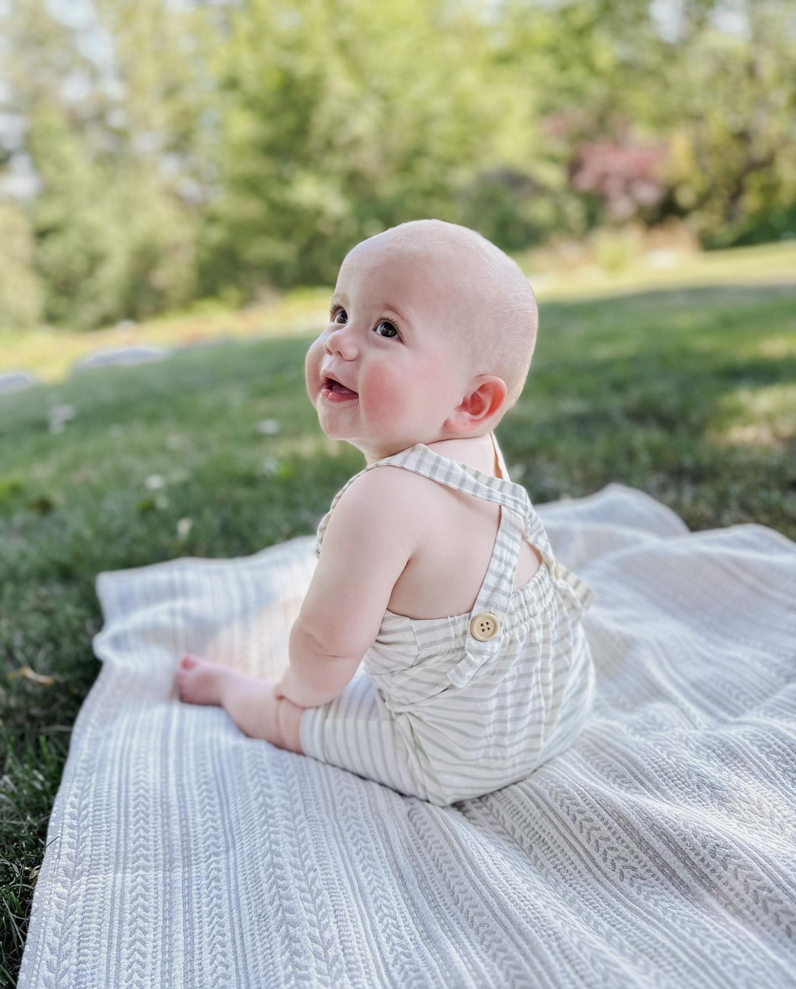 Baby girl sitting and smiling on a blanket on the grass outside