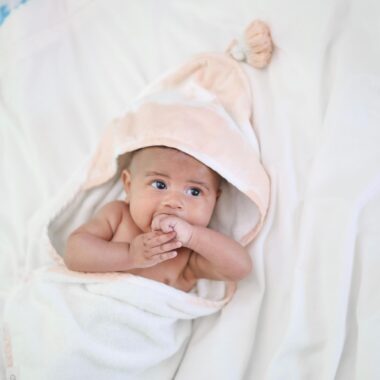 Baby wrapped in a hooded towel and eating his hand