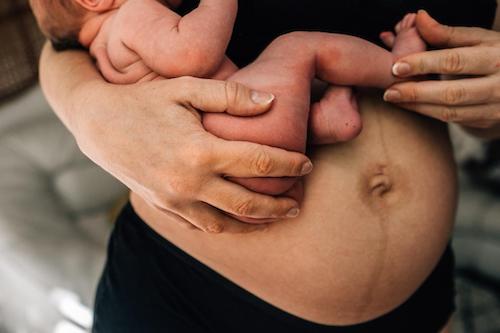 Close up of a newborn wrapped around the side of a mom's belly