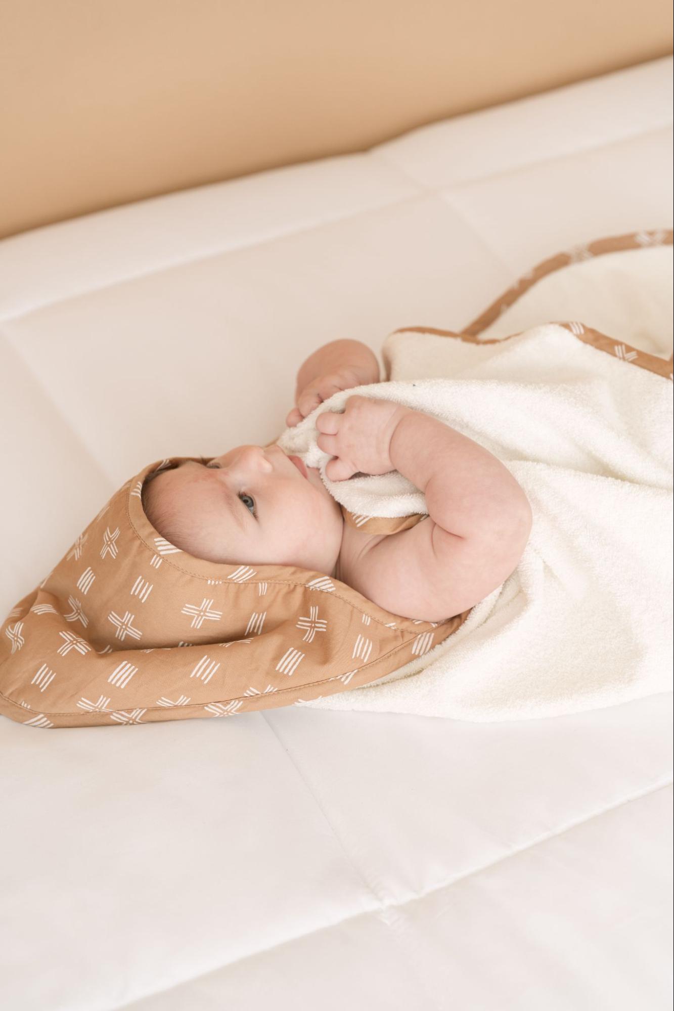 Baby lying down wrapped with a hooded towel