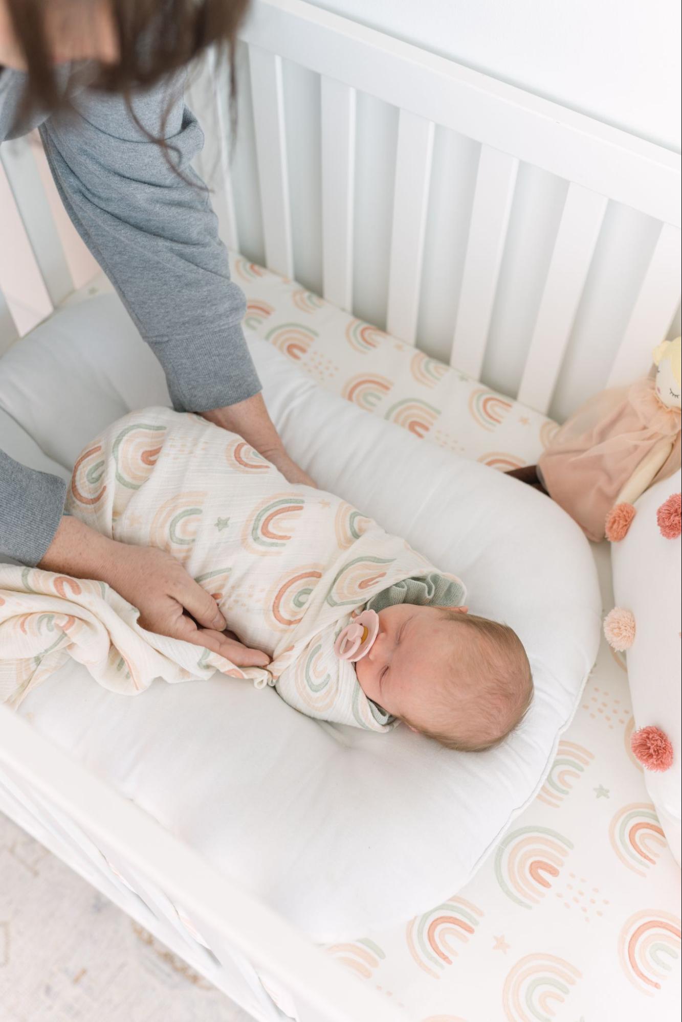 Parent placing swaddled baby into their crib