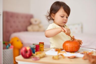 Toddler girl painting a pumpkin in a bedroom