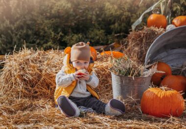 Toddler boy eating an apple while sitting on a haystack