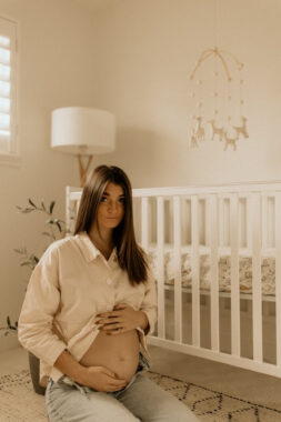 Woman holding her pregnant belly while sitting next to a crib