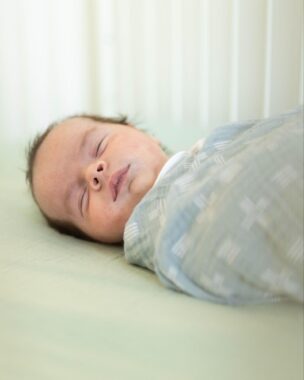 Close up of a sleeping baby swaddled in a crib