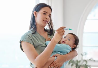 Mom carrying her baby and looking at a thermometer