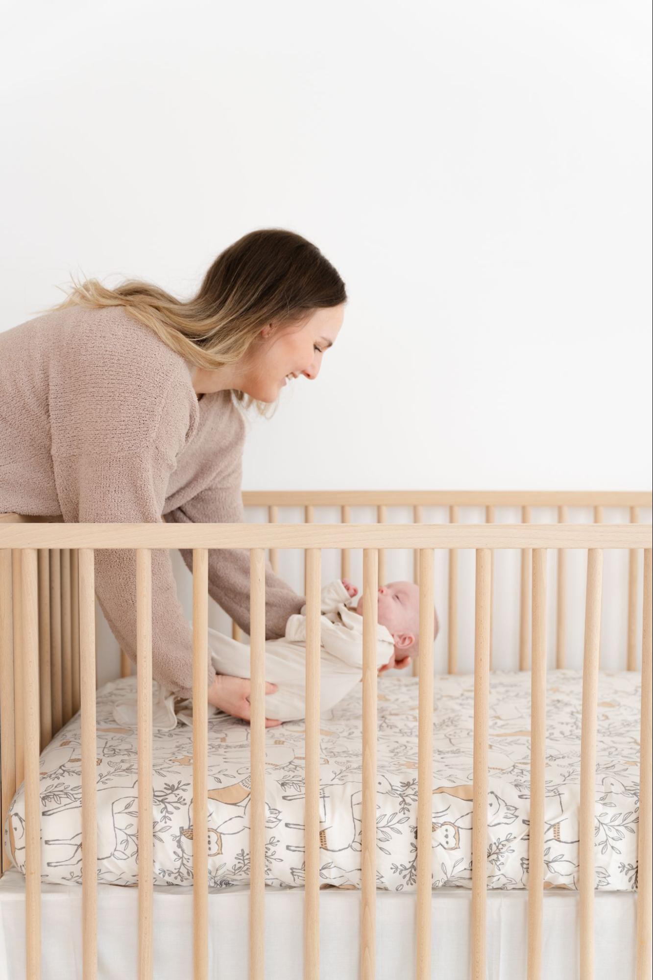 Mother lying her sleeping baby in a crib