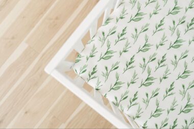 Corner of a white crib with a leaf fitted sheet