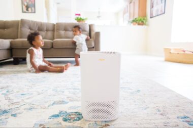 Air purifier on the floor in a living room with 2 babies playing in the back