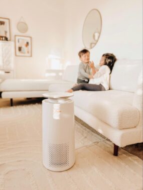 Air purifier on a rug next to 2 children sitting on a couch