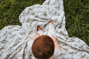 Bird's eye view of a baby sitting on a swaddle blanket on the grass