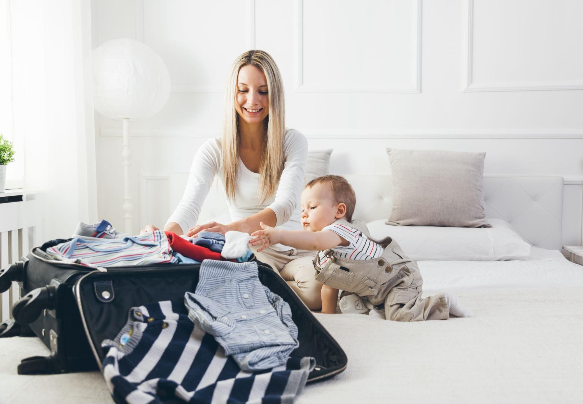 Baby and mom on a bed packing a suitcase
