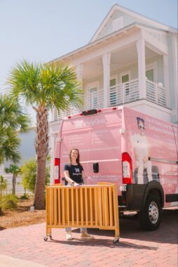 Employee holding a rentable crib in front of a work car