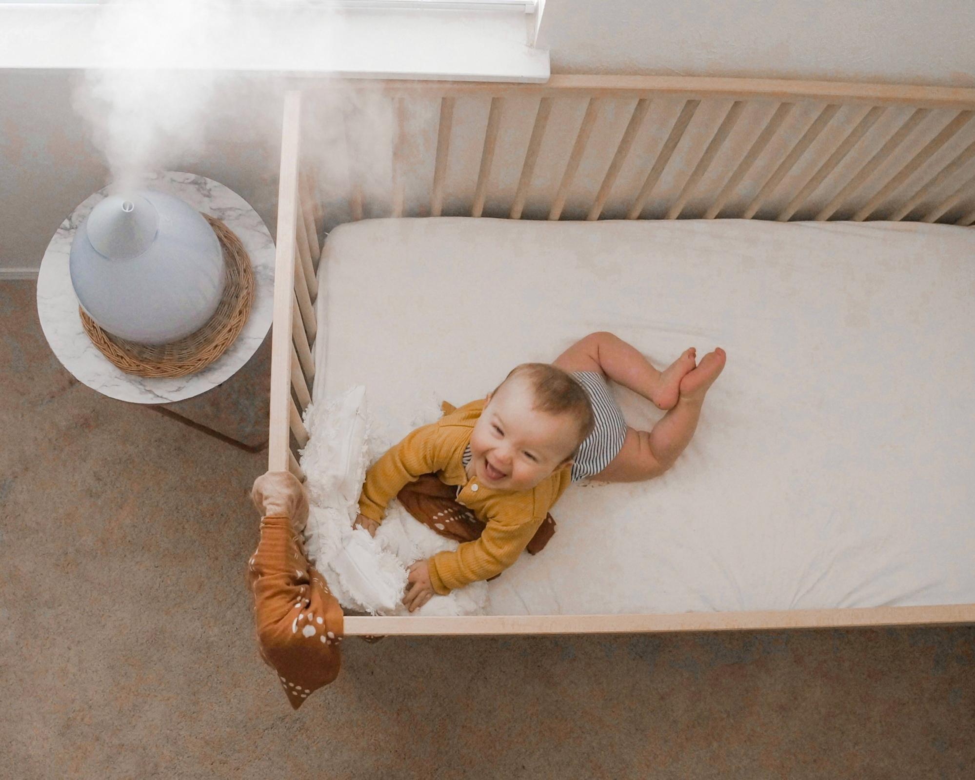 Baby in a crib doing tummy time next to a humidifier on a table