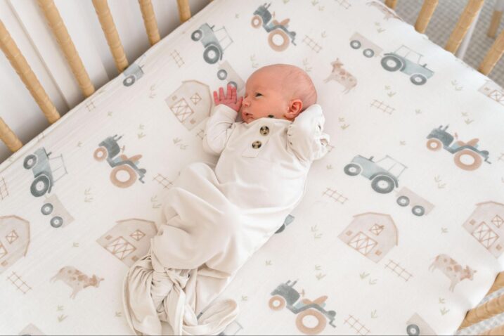Baby in a knotted gown lying down in a crib with a tractor sheet