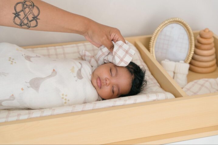 Mother wiping a sleeping swaddled baby on the forehead