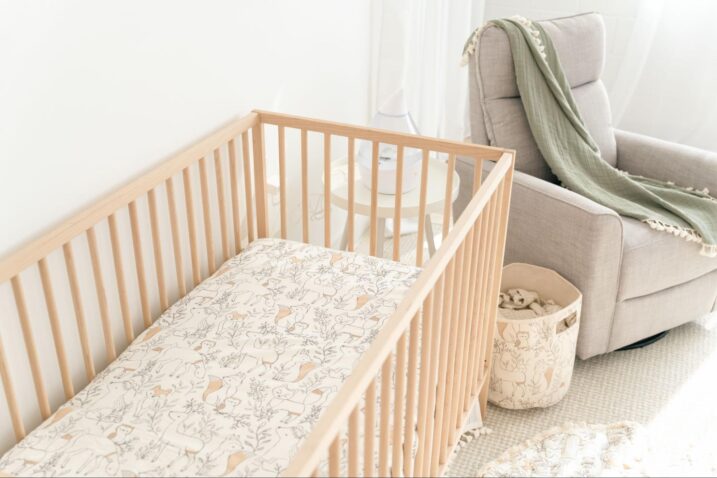 Baby crib next to a gray glider and storage basket