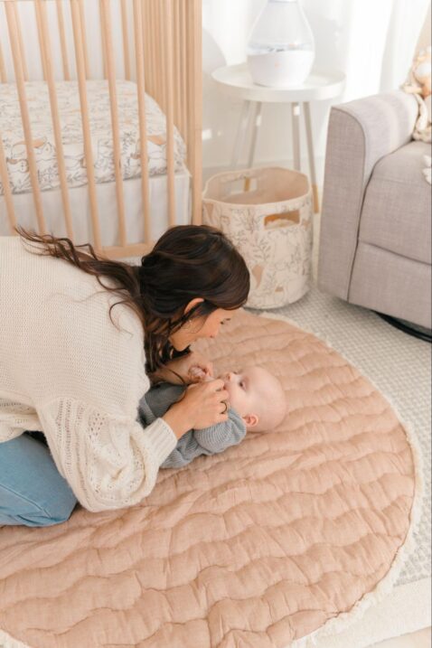 Mom playing with her baby who is lying down on a playmat